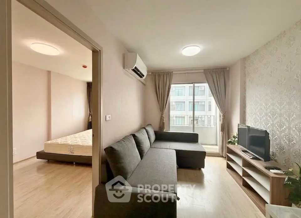 Modern living room with grey sectional sofa and TV, adjacent to a bedroom with natural light.