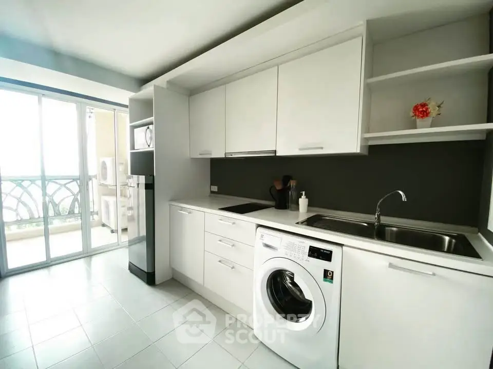 Modern kitchen with sleek white cabinets and washing machine, featuring balcony access.