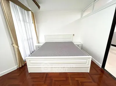 Spacious bedroom with elegant wooden flooring and natural light from large windows.