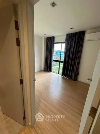 Spacious bedroom with wooden flooring and large window for natural light