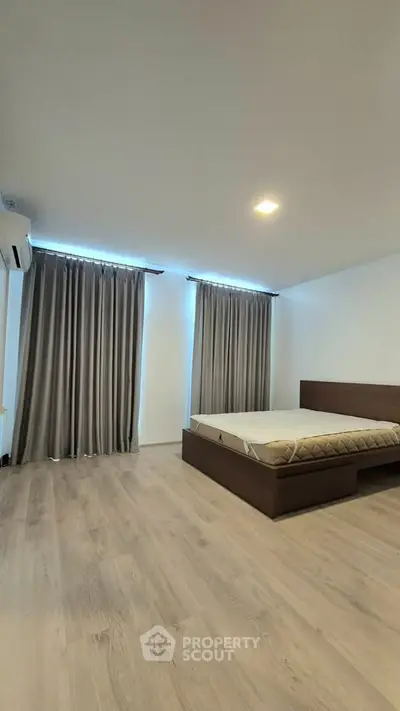 Spacious bedroom with modern design and wooden flooring, featuring large windows with elegant curtains.