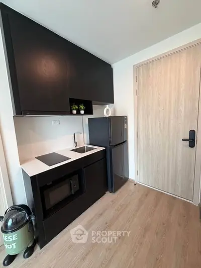 Modern compact kitchen with sleek black cabinets and appliances, featuring a microwave and fridge.