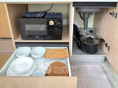Modern kitchen storage with microwave, cookware, and organized dishware in sleek cabinetry.