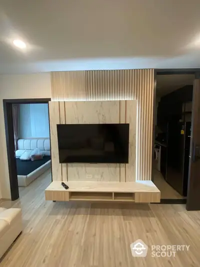 Modern living room with elegant marble TV wall, sleek wooden flooring, and contemporary furnishings, leading to a cozy bedroom and a well-equipped kitchen.