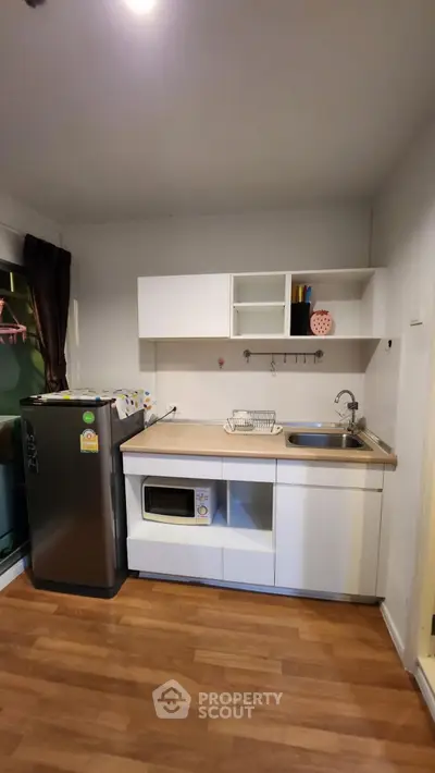 Modern kitchen with sleek white cabinets, stainless steel fridge, and microwave on wooden flooring.
