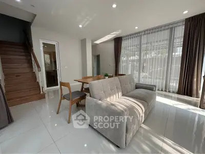 Modern living room with sleek sofa and dining area, featuring large windows and natural light.
