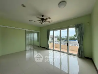 Spacious living room with large windows and balcony access, featuring a ceiling fan and serene green walls.