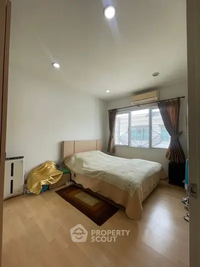 Cozy bedroom with natural light and wooden flooring, featuring a comfortable bed and air conditioning.