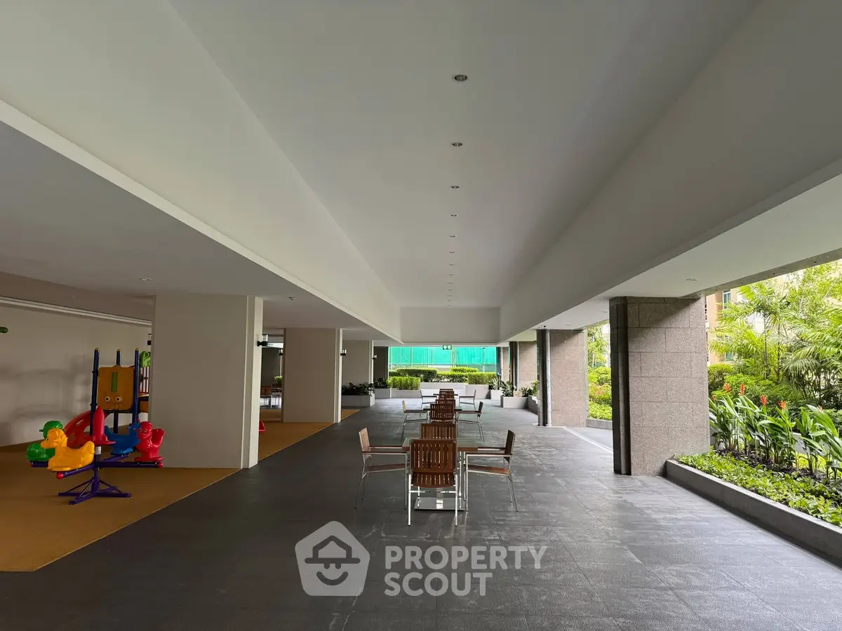 Spacious covered outdoor area with seating and children's play equipment in modern residential complex.