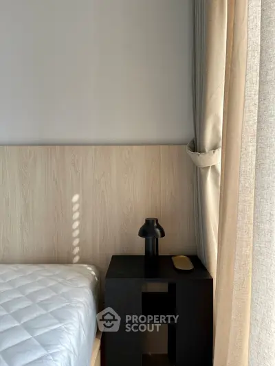 Cozy bedroom corner with natural light, featuring a modern black nightstand and elegant curtains.