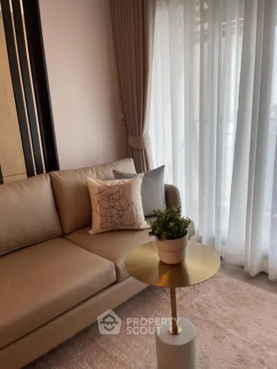 Elegant living room with beige sofa, stylish cushion, and gold accent table near sheer curtains.