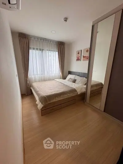 Cozy bedroom with large window and mirrored wardrobe in modern apartment.