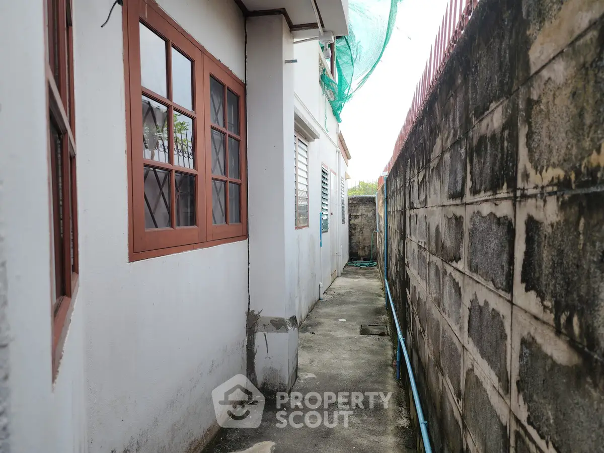 Narrow exterior walkway beside a residential building with concrete walls and windows.