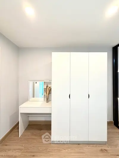 Modern bedroom with sleek white wardrobe and vanity set on wooden flooring.