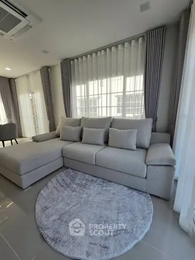 Modern living room with stylish gray sofa and round rug, featuring elegant floor-to-ceiling windows.