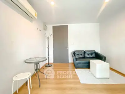Modern living room with sleek black sofa, glass table, and wooden flooring in a minimalist apartment.
