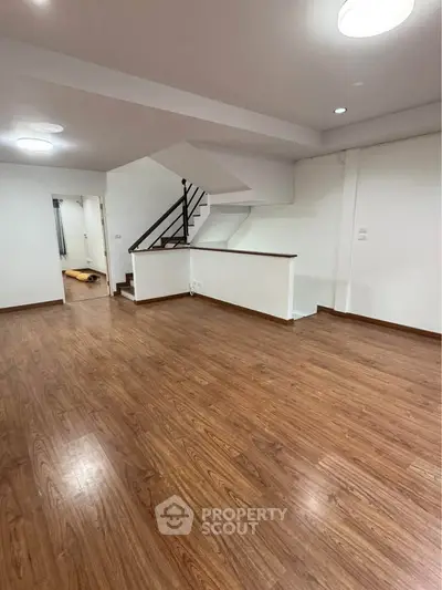 Spacious open-plan living area with wooden flooring and modern staircase, perfect for family gatherings.