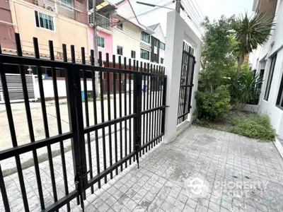 Modern townhouse entrance with secure black metal gate and paved driveway