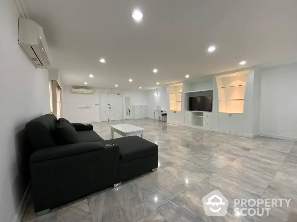 Spacious modern living room with sleek black sofa and built-in entertainment center.