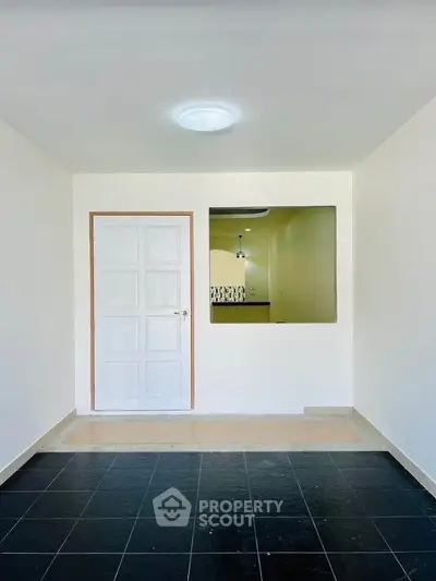 Minimalist interior with white door and open kitchen layout, featuring sleek black tiles and modern lighting.