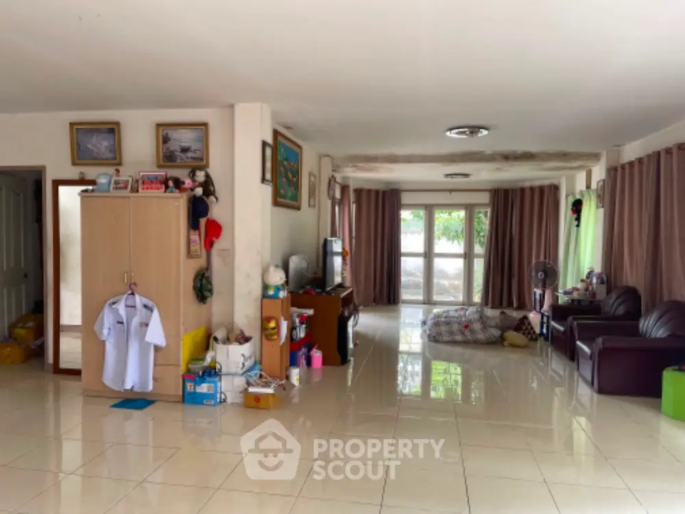 Spacious living room with glossy tiled flooring, large windows draped with curtains, and an array of personal items and furniture.