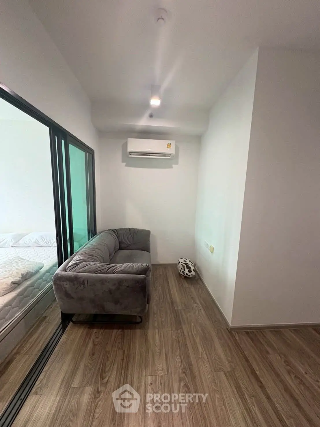 Cozy small living area with modern sofa and air conditioning, adjacent to a bedroom with glass sliding doors.