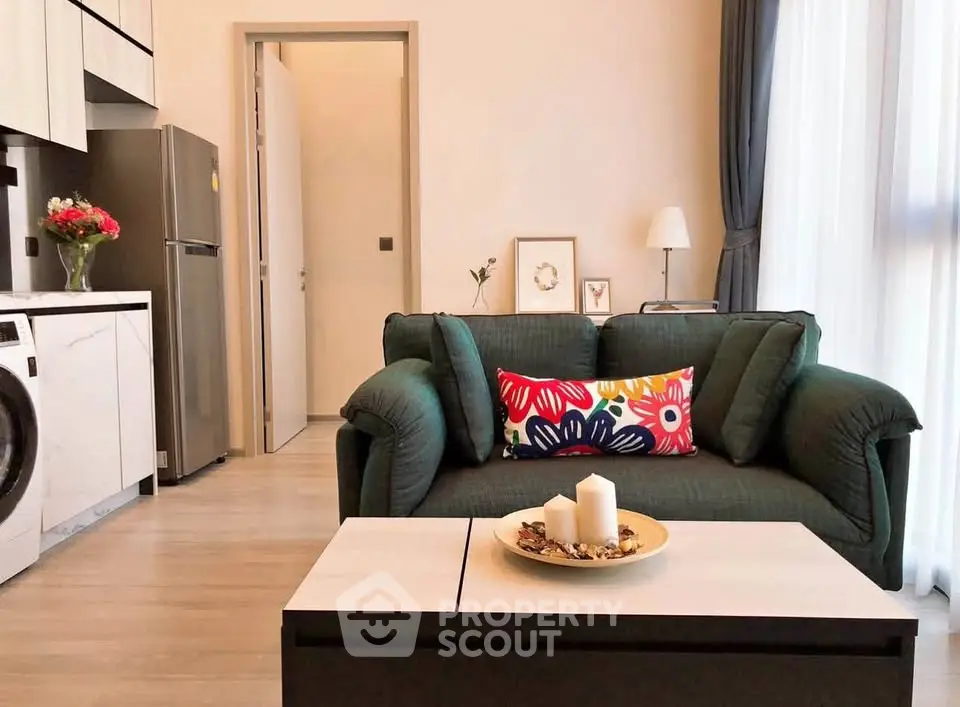 Modern living room with stylish sofa, vibrant decor, and sleek kitchen appliances in open layout.