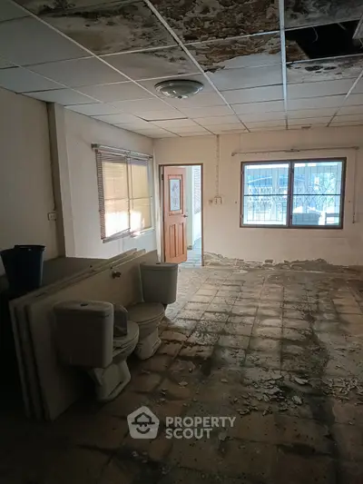 Dilapidated interior space with exposed ceiling and damaged flooring, potential for renovation.
