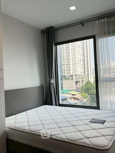 Modern bedroom with large window offering city view in high-rise apartment.