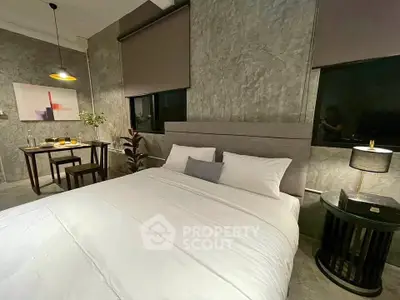 Modern bedroom with stylish decor and cozy dining area, featuring concrete walls and ambient lighting.