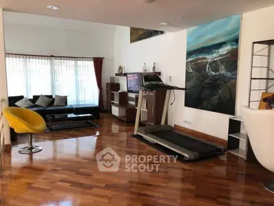 Spacious living room with modern decor and treadmill, featuring hardwood floors and large windows.