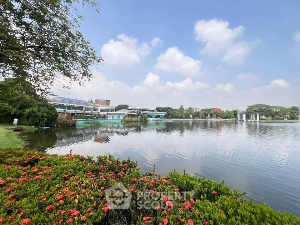 Scenic view of a serene lake with lush greenery and modern buildings in the background.