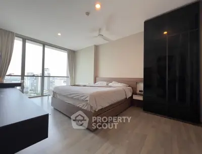 Spacious bedroom with city view, modern furnishings, and large windows.