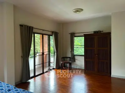 Spacious bedroom with wooden flooring and balcony access in serene setting