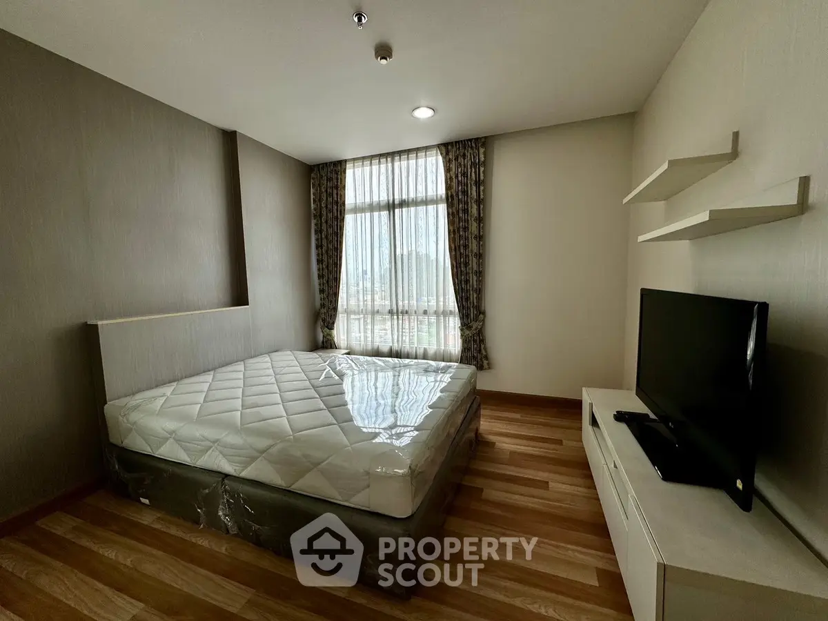 Modern bedroom with large window and TV, featuring stylish wooden flooring and elegant curtains.