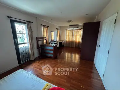 Spacious bedroom with wooden flooring and natural light, featuring a desk and large windows.