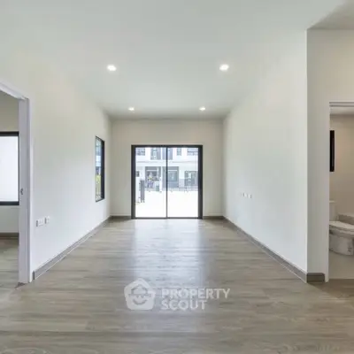 Spacious empty room with wooden flooring and large window, ideal for customization.