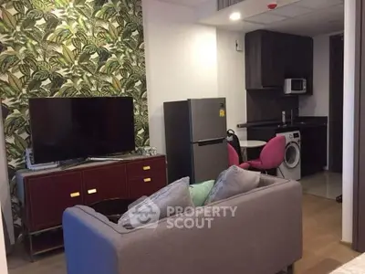 Modern living room with tropical wallpaper, TV, and compact kitchen featuring fridge and washing machine.