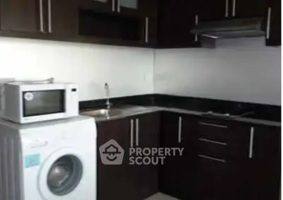 Modern kitchen with dark cabinets, washing machine, and microwave, perfect for urban living.