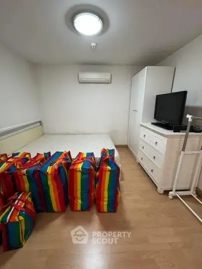Cozy bedroom with minimalist decor and colorful storage bags, featuring a TV and air conditioning.