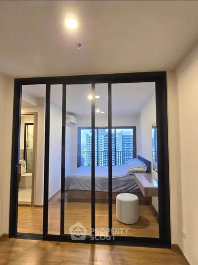 Modern bedroom with sliding glass doors and city view, featuring wooden flooring and contemporary decor.