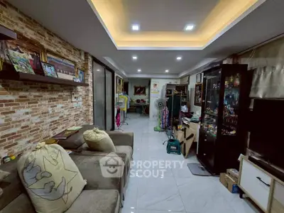 Spacious living room with modern lighting and brick accent wall, featuring cozy seating and display cabinets.