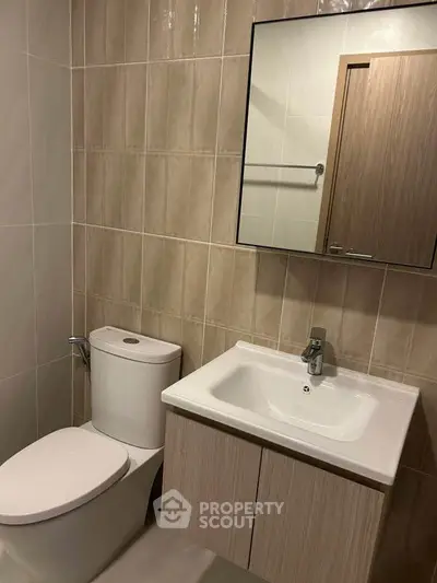 Modern bathroom with sleek fixtures and neutral tiles, featuring a compact vanity and mirror.
