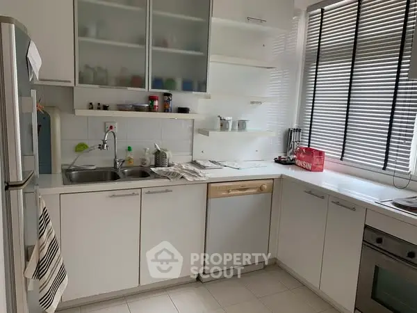 Modern kitchen with sleek cabinetry and natural light, featuring a dishwasher and oven.