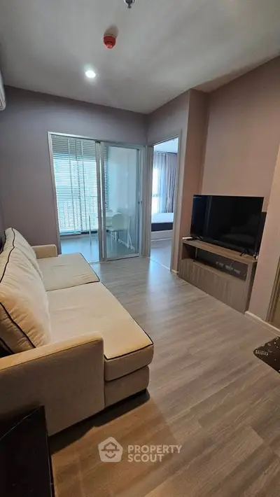 Modern living room with cozy sofa and TV, featuring sliding glass doors leading to a bright bedroom.