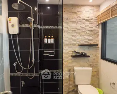 Modern bathroom with sleek black tiles and stone accent wall, featuring a shower and toilet.