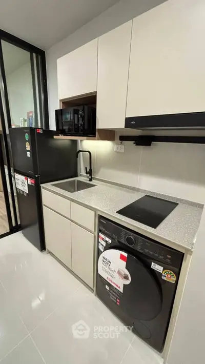 Modern kitchen with sleek appliances and compact design, featuring a washing machine and induction cooktop.