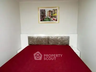 Cozy bedroom with vibrant red bedding and framed artwork, perfect for a comfortable living space.