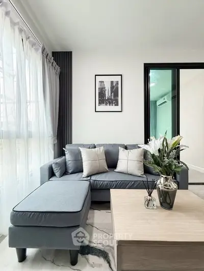 Modern living room with stylish gray sofa, elegant decor, and natural light from large windows.