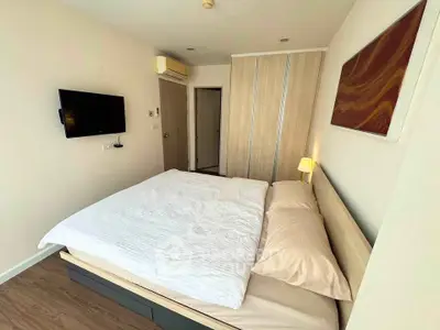 Modern bedroom with stylish decor and ample natural light, featuring a cozy bed and wall-mounted TV.
